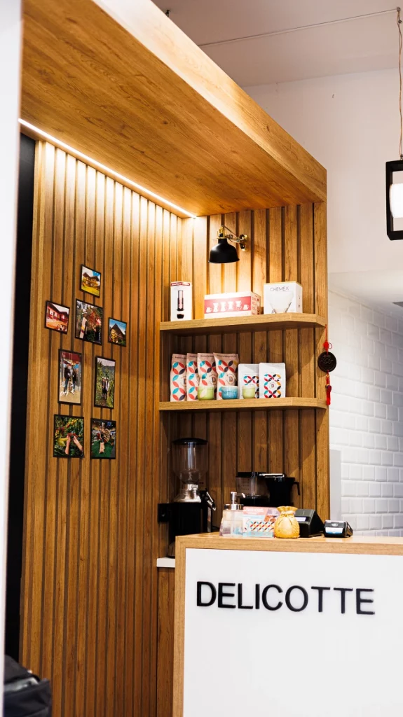 Mostrador de tienda de café de especialidad con estantes de madera que exhiben paquetes de café y decoración cálida.