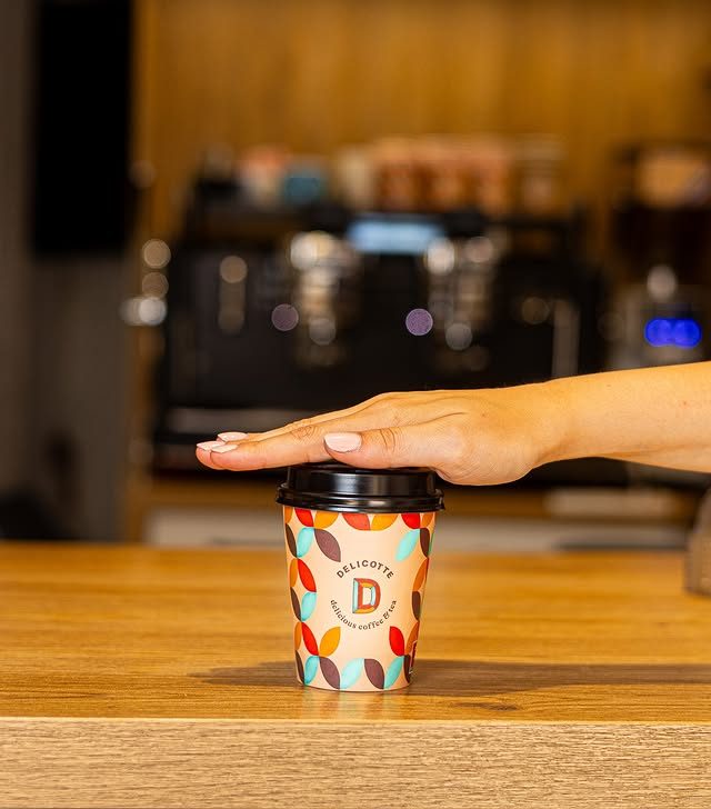 Vaso de café para llevar con diseño colorido de la tienda de café de especialidad, con una mano colocando la tapa.